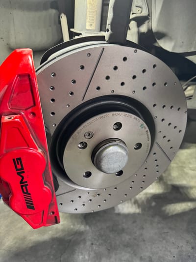 AMG front brake caliper and slotted rotor being fitted during a brake replacement.