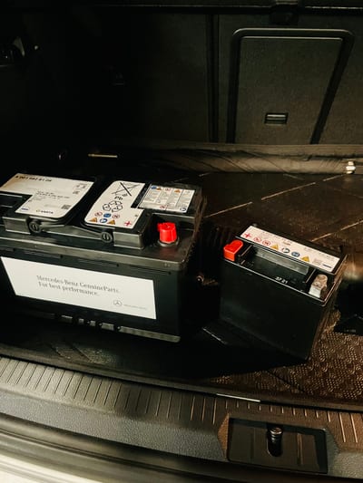 Battery tester clamped to a Mercedes battery with multimeter readings being recorded.